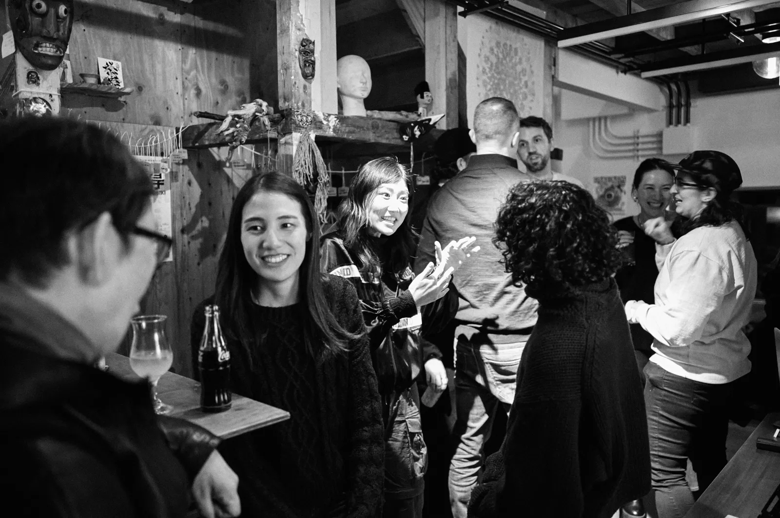 Guests chat and laugh over drinks at a Jinny artists mixer, in black and white